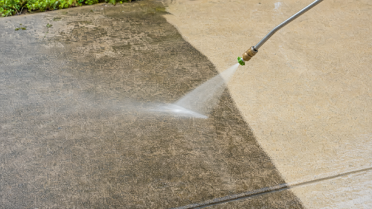 Pressure washer cleaning a grimy concrete driveway, showing a clear line between dirty and clean concrete
